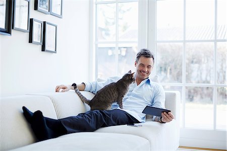 domestic cat - Man relaxing on sofa using digital tablet with cat Stock Photo - Premium Royalty-Free, Code: 649-07064536