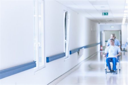 Nurse pushing patient in wheelchair down corridor Photographie de stock - Premium Libres de Droits, Code: 649-07064708