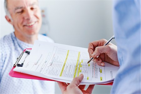 Nurse completing paperwork, patient in background Stock Photo - Premium Royalty-Free, Code: 649-07064703