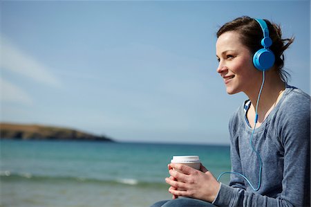 Young woman at coast with coffee and earphones Stock Photo - Premium Royalty-Free, Code: 649-07062995