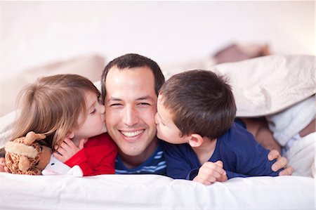 father son bedroom - Son and daughter kissing fathers cheek under duvet Stock Photo - Premium Royalty-Free, Code: 649-07063634