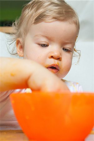 Baby girl with hand in orange bowl Stock Photo - Premium Royalty-Free, Code: 649-07118197