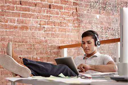 Young man using digital tablet wearing headphones, feet up Photographie de stock - Premium Libres de Droits, Code: 649-07118341