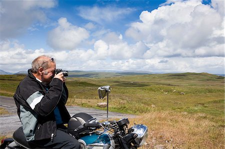 Senior male motorcyclist taking a photograph of scene Stock Photo - Premium Royalty-Free, Code: 649-07118646