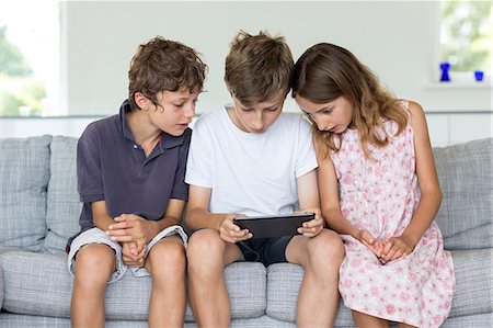 Brothers and sister on sofa looking at digital tablet Stock Photo - Premium Royalty-Free, Code: 649-07118651
