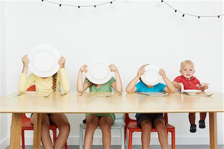 preteen plate - Four children sitting at table, three covering faces with plates Stock Photo - Premium Royalty-Free, Code: 649-07119711