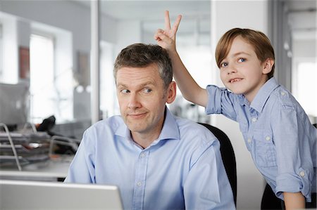 paper work - Father using laptop, son making peace sign behind his head Photographie de stock - Premium Libres de Droits, Code: 649-07119817