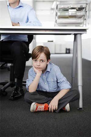 Boy sitting on floor with businessman working at desk Stock Photo - Premium Royalty-Free, Code: 649-07119820