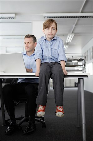 Boy sitting on desk with businessman working Stock Photo - Premium Royalty-Free, Code: 649-07119821