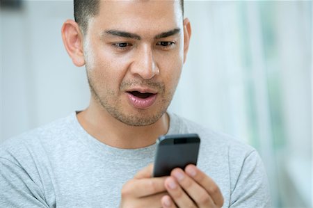 Mid adult man looking surprised at smartphone Stock Photo - Premium Royalty-Free, Code: 649-07238270