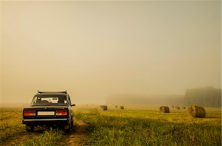 Car driving through field of haystacks on overcast day Stock Photo - Premium Royalty-Free, Code: 649-07238441
