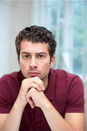 Young man resting chin on clasped hands Photographie de stock - Premium Libres de Droits, Code: 649-07238893