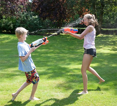 Brother and sister play fighting with water guns in garden Stock Photo - Premium Royalty-Free, Code: 649-07239176