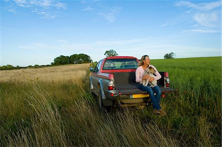 simsearch:649-07239644,k - Woman sitting on back of pick up truck in a field, holding a dog Photographie de stock - Premium Libres de Droits, Code: 649-07239433