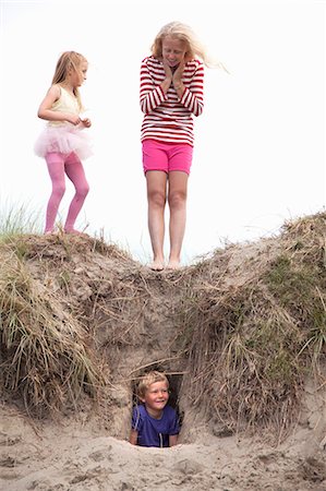 Boy hiding in hole in dunes with girls above, Wales, UK Photographie de stock - Premium Libres de Droits, Code: 649-07239488