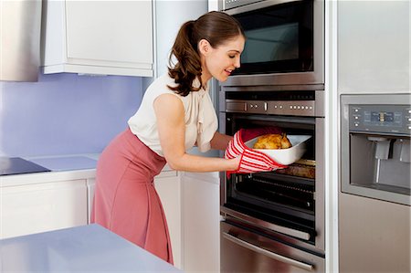 Young woman taking roasting dish out of oven Stock Photo - Premium Royalty-Free, Code: 649-07239849