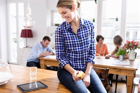 Young woman eating apple looking at tablet screen smiling, people in background Photographie de stock - Premium Libres de Droits, Code: 649-07279568