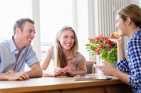 simsearch:649-07279563,k - Three young people sitting at a table talking and smiling Photographie de stock - Premium Libres de Droits, Code: 649-07279569