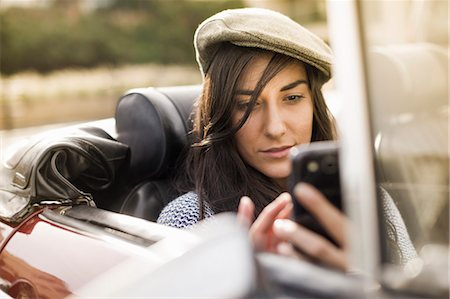 Young woman wearing flat cap in convertible using smartphone Photographie de stock - Premium Libres de Droits, Code: 649-07279671