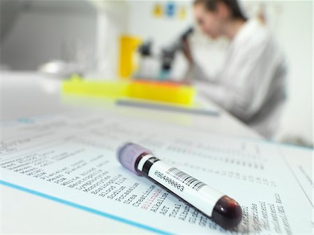 Blood tube sitting on blood results with technician at microscope in lab Photographie de stock - Premium Libres de Droits, Code: 649-07279800