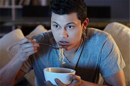 Young man eating noodles and watching tv Stock Photo - Premium Royalty-Free, Code: 649-07280697