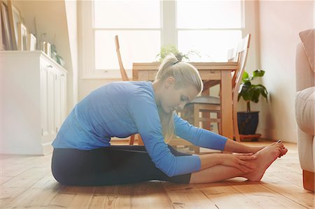 Young woman sitting on floor leaning forwards touching toes Stock Photo - Premium Royalty-Free, Code: 649-07280719