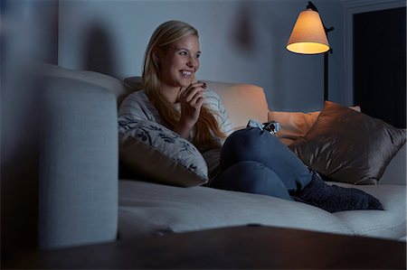 simsearch:649-07280728,k - Young woman sitting on sofa, watching tv, eating chocolate Stock Photo - Premium Royalty-Free, Code: 649-07280754