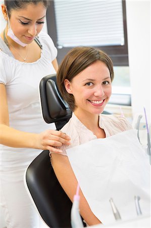 female dentist looking at camera - Young woman in dentists chair with dental nurse Stock Photo - Premium Royalty-Free, Code: 649-07280875