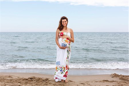 pregnant lady standing - Pregnant woman standing on beach, hands on stomach Stock Photo - Premium Royalty-Free, Code: 649-07436421