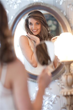 Portrait of young woman looking in wall mirror Stock Photo - Premium Royalty-Free, Code: 649-07436589