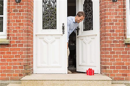 front door - Mid adult man with gift on front doorstep Stock Photo - Premium Royalty-Free, Code: 649-07436822