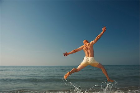 simsearch:649-07281022,k - Mid adult man jumping outstretched over sea Fotografie stock - Premium Royalty-Free, Codice: 649-07437187