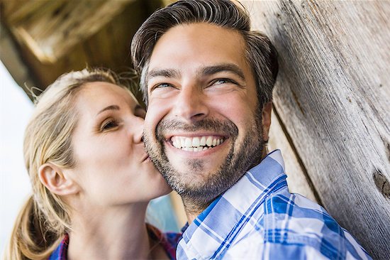 Woman kissing man's cheek outside wooden shack Stock Photo - Premium Royalty-Free, Image code: 649-07437325