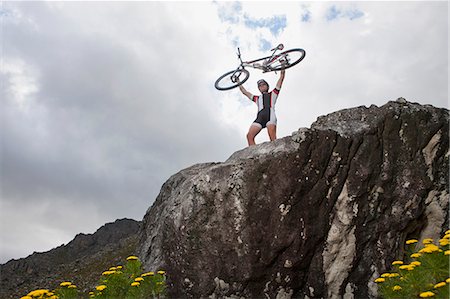 Young man holding up mountain bike on top of rock Stock Photo - Premium Royalty-Free, Code: 649-07520857