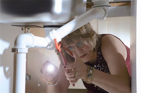 Senior woman in evening wear fixing pipes under kitchen sink Foto de stock - Sin royalties Premium, Código: 649-07521044