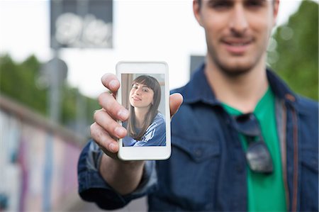 Young man holding up smartphone with photograph of girlfriend Stock Photo - Premium Royalty-Free, Code: 649-07560145