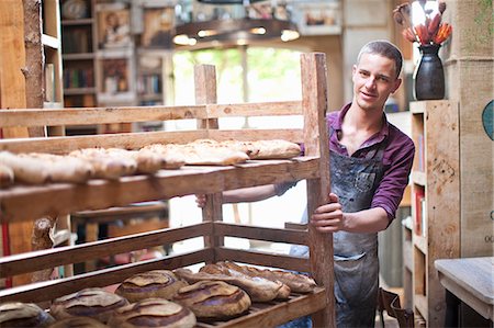 Portrait of young male baker with shelves of fresh bread Stockbilder - Premium RF Lizenzfrei, Bildnummer: 649-07585068