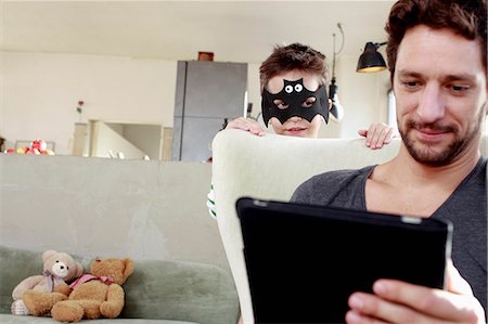 Masked son distracting father from digital tablet Photographie de stock - Premium Libres de Droits, Code: 649-07585457