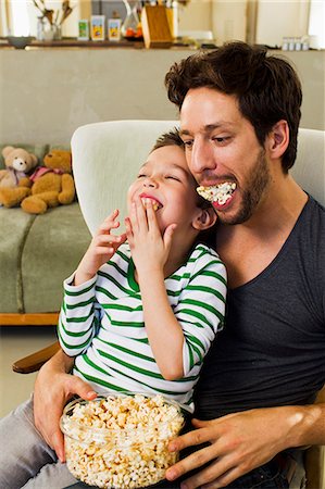 dad son playing indoors - Father and young son with mouthfuls of popcorn Stock Photo - Premium Royalty-Free, Code: 649-07585485