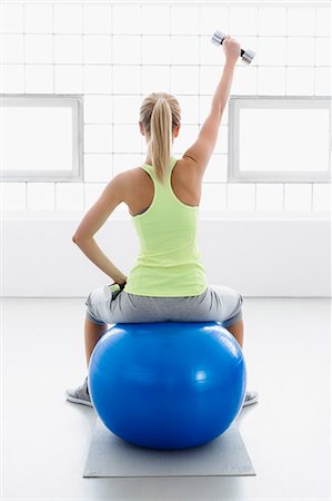 physically fit - Young woman sitting on exercise ball, rear view, lifting weights Stock Photo - Premium Royalty-Free, Code: 649-07585505