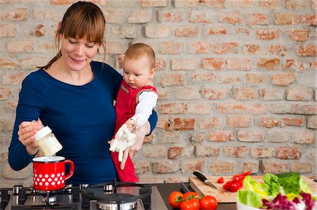 simsearch:6108-06167734,k - Mother carrying baby daughter whilst preparing lunch Photographie de stock - Premium Libres de Droits, Code: 649-07647972