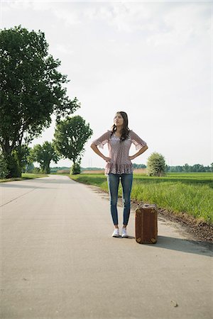 Young woman standing on country road with suitcase Stock Photo - Premium Royalty-Free, Code: 649-07648343