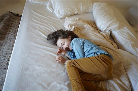 Giggling young girl curled up on bed Stock Photo - Premium Royalty-Free, Code: 649-07648607