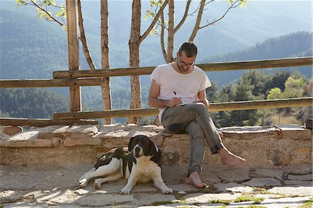 Mid adult man with dog writing notes on patio Stock Photo - Premium Royalty-Free, Code: 649-07648616
