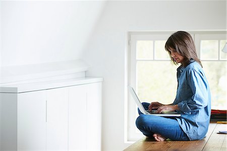 Businesswoman sitting on desk, legs crossed, using laptop Stock Photo - Premium Royalty-Free, Code: 649-07710426