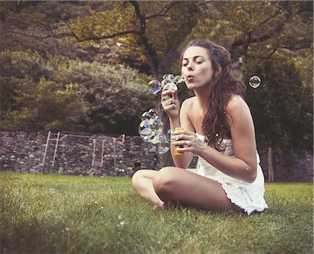 simsearch:649-07709901,k - Young woman sitting in field blowing bubbles Stock Photo - Premium Royalty-Free, Code: 649-07710822