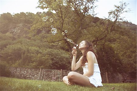 simsearch:649-07709901,k - Young woman sitting cross legged in field blowing bubbles Stock Photo - Premium Royalty-Free, Code: 649-07710823