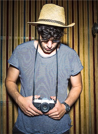 people holding camera slr - Portrait of young man looking down at vintage camera Stock Photo - Premium Royalty-Free, Code: 649-07736498