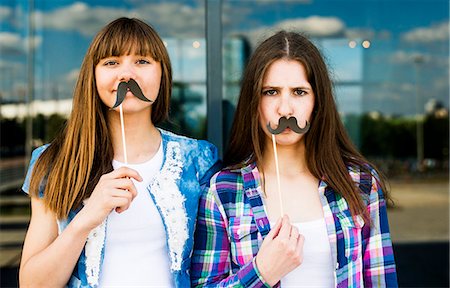 funny people happy caucasian - Portrait of two young women holding up mustache costume masks Foto de stock - Sin royalties Premium, Código: 649-07736855