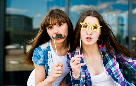 simsearch:649-07436665,k - Portrait of two young women holding up mustache and specs costume masks Fotografie stock - Premium Royalty-Free, Codice: 649-07736852